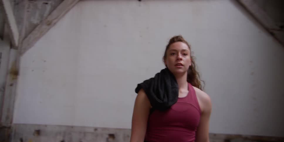 A woman picks up a camera on a tripod puts a jacket over her shoulder and leaves