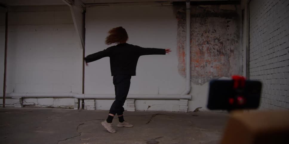 Female dancer dancing alone in studio records herself with a smartphone on a stand