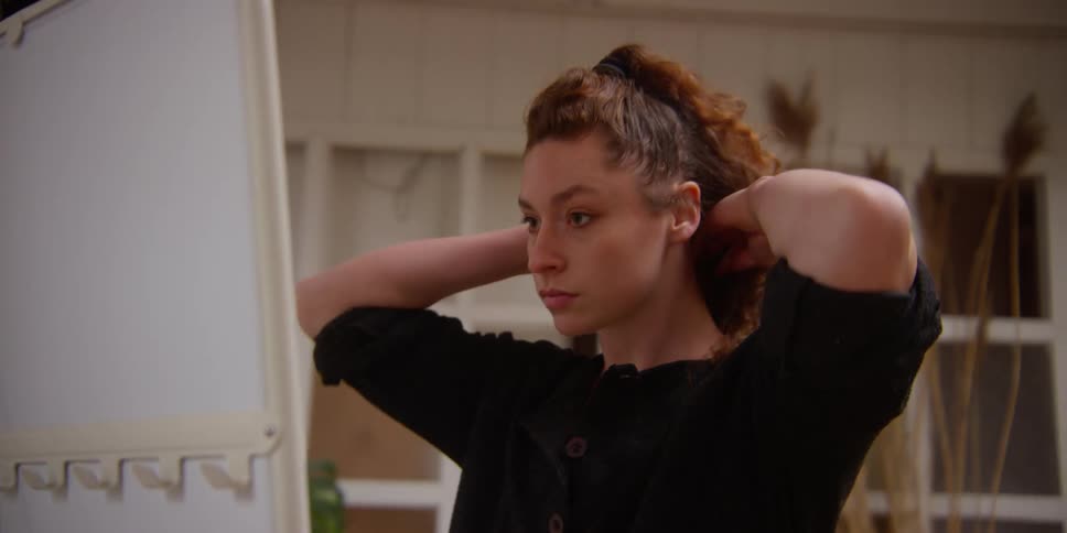 Woman with curly hair and a black sweater looks in the mirror