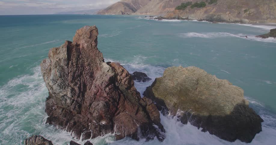 Jagged rocks protrude from above the ocean surface as waves crash into it