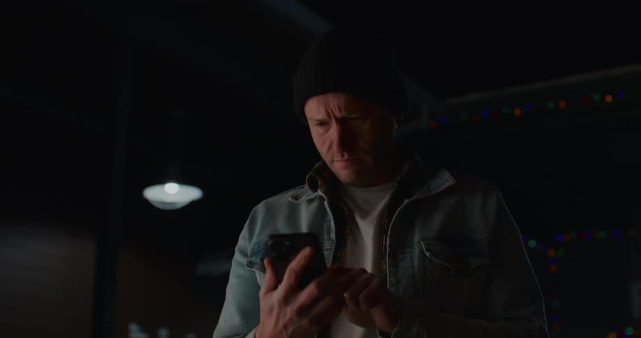 A man typing on a cell phone during the cold night