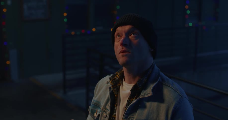 A man wearing a denim jacket and beanie looks upwards