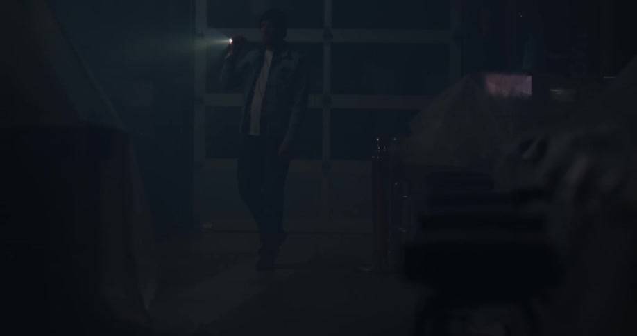 A man is searching around with a flash light in the dark