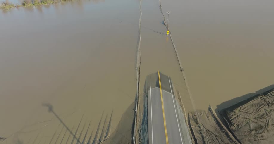 A portion of a rural roadway is submerged beneath floodwaters