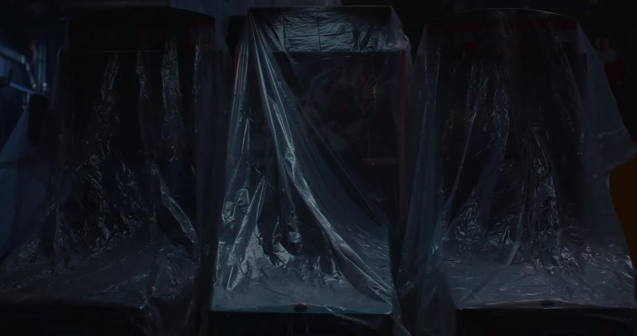 Close up of an arcade or pinball machine under plastic covers inside a dark warehouse