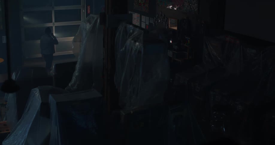 Man entering a dark warehouse with machines wrapped in plastic