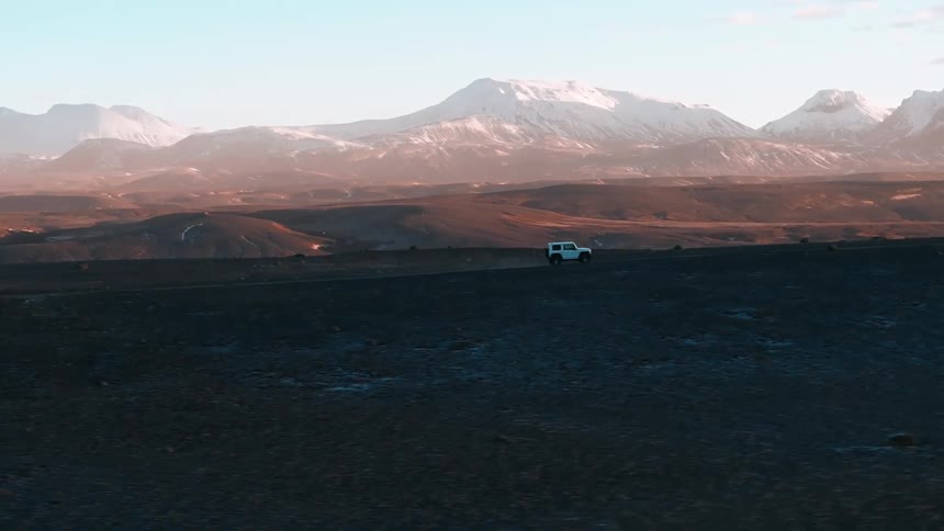 A car driving on a rural road and on the horizon there are big mountains