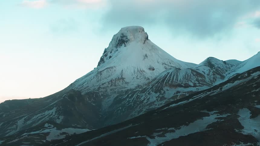 A snowcapped mountain peak is illuminated by the soft morning light