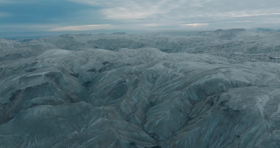 A vast and rugged landscape of barren mountains under clouds