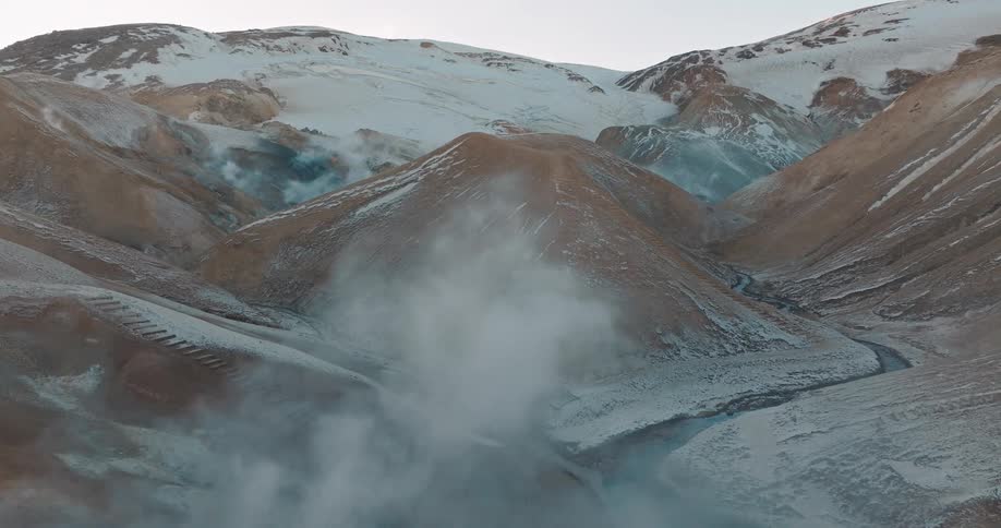 Steam raises from geysers near a mountain range