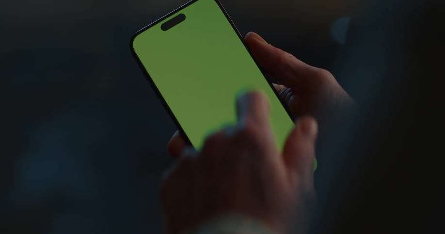 An adult works on a smartphone with a green screen