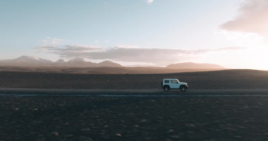 Aerial of a car driving down a deserted road during sunset