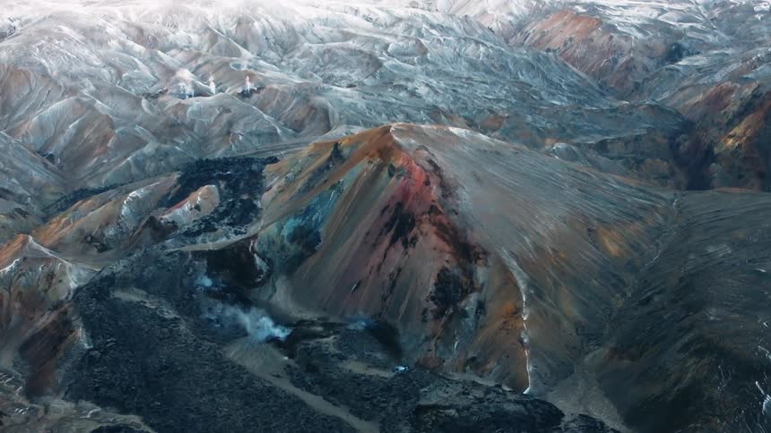 An aerial view of a mountainous landscape reveals that some are covered in snow