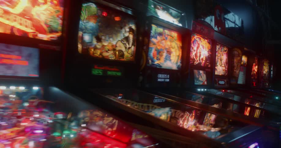 A row of colorful and illuminated pinball machines in a dark arcade