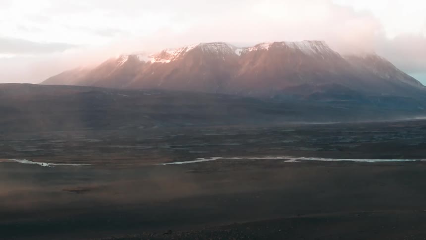 A serene landscape of a plain with a large mountain range in the background at sunset