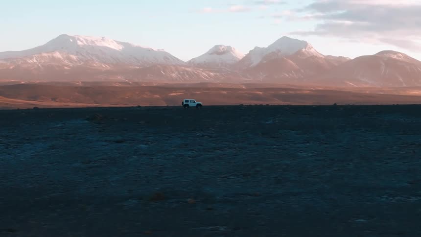 Aerial of a car driven through the desert with mountains in the background