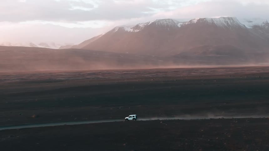 Aerial view of a white allterrain vehicle driving near misty snowcapped mountains