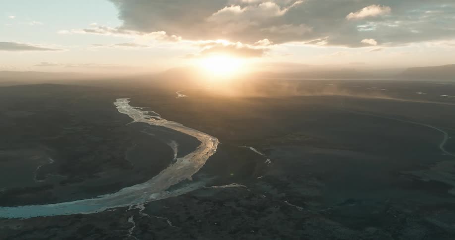 The sun is set low in the sky above a landscape with a large river flowing through it