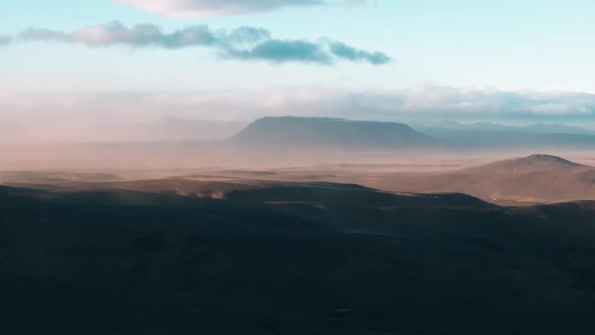 A landscape of rolling hills and distant mountains under a sky with soft clouds