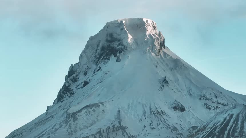 Snow covered mountain peak high in a cloudy sky