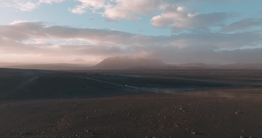 Aerial view of a vehicle driving on the plains next to a misty mountain at morning