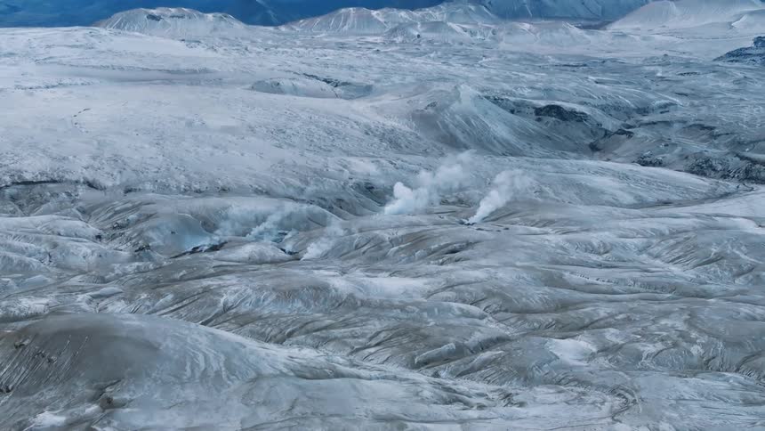 Aerial view of geothermal steam columns rising on a snow covered rugged terrain