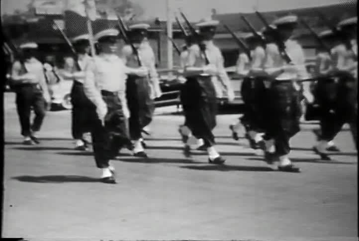 Young boys carrying rifles march in a parade