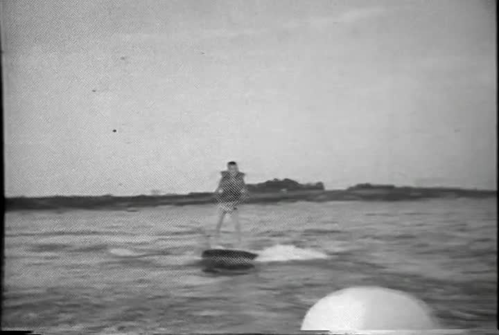 A person in a life vest rides a board across the water