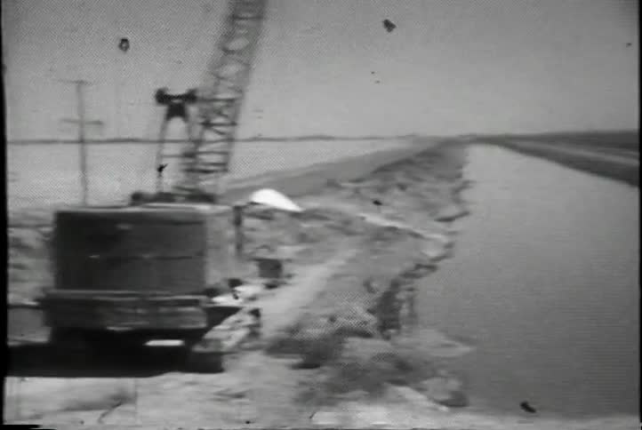 A vehicle passes by a canal and a construction crane as it travels