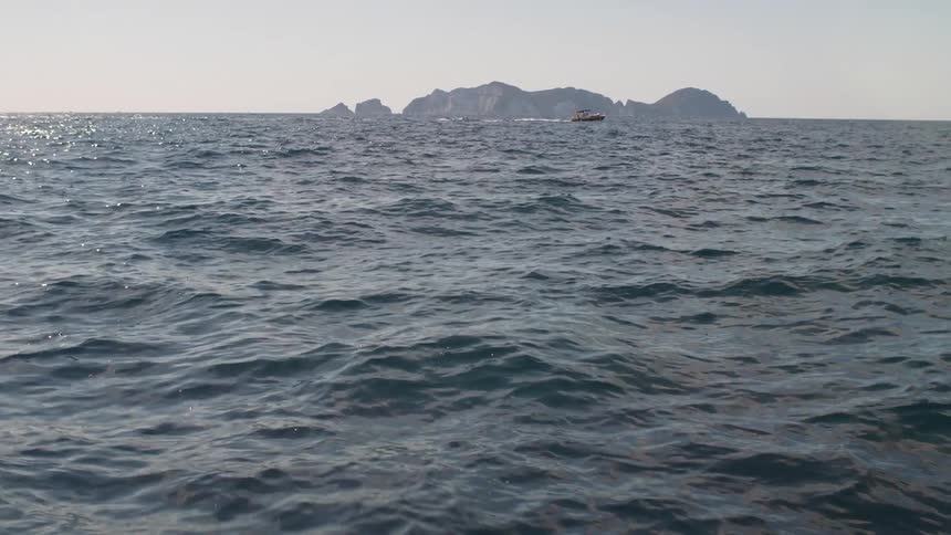 A boat sailing in a sea with some waves and there is an island in the background