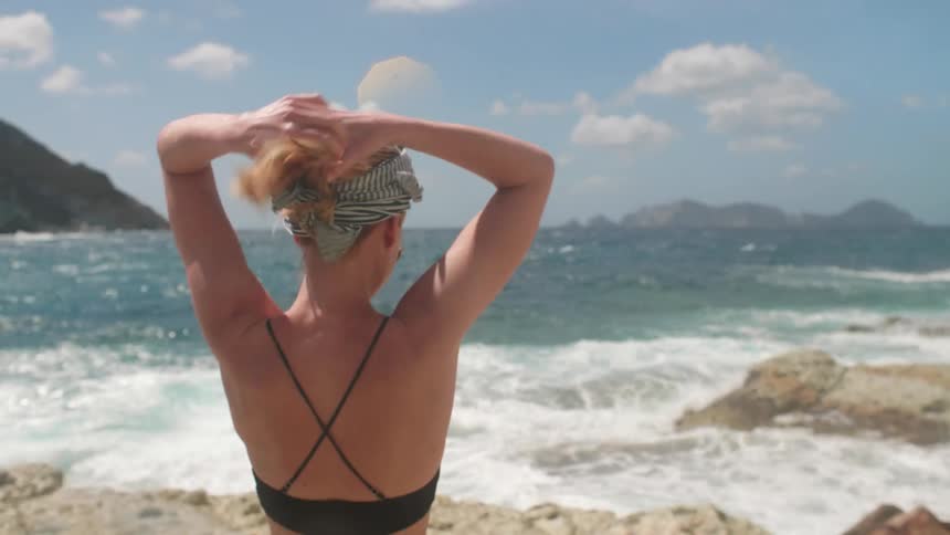 A woman puts her hair in a bun on the beach