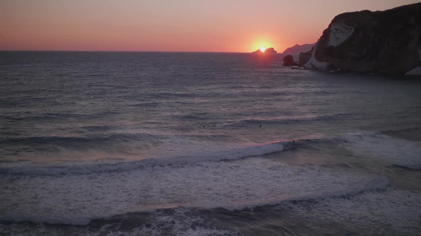 Aerial of people surfing on a beach during sunset