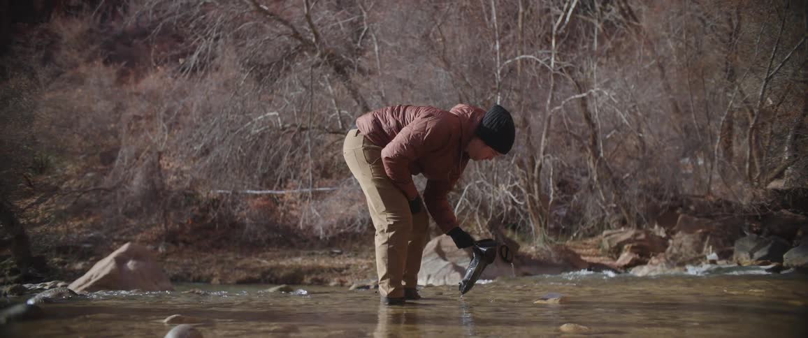 A man filling a bottle with water from a river