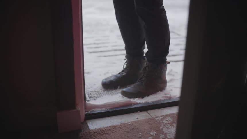 A person stamps snow off of their boots at a doorway