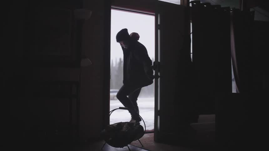 A man opens his front door and brings in a bundle of firewood