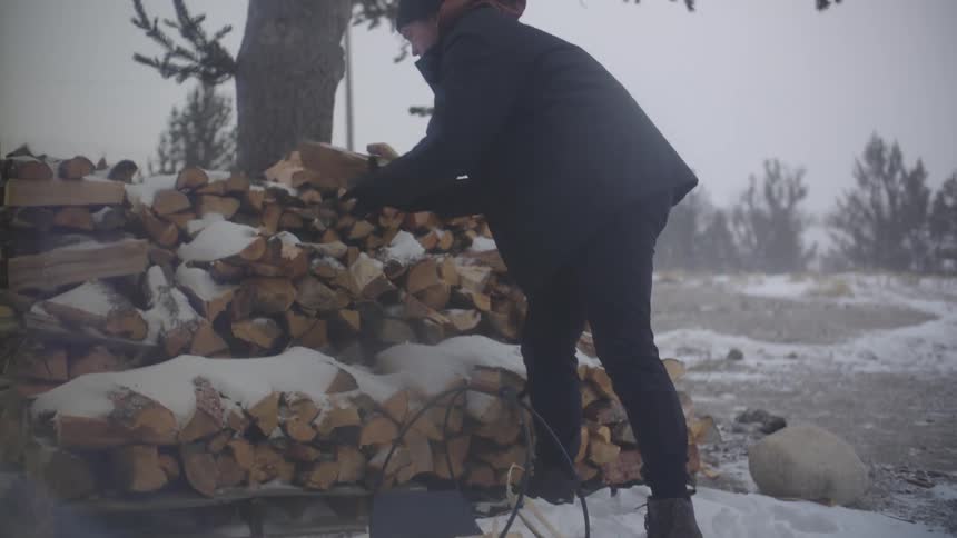 Man picking up cut firewood putting it in a metal basin on a snowy day