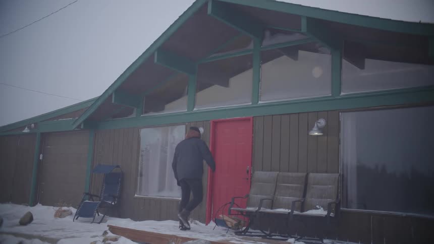 Man cleaning his feet and opening the door to enter a house on a snowstorm day