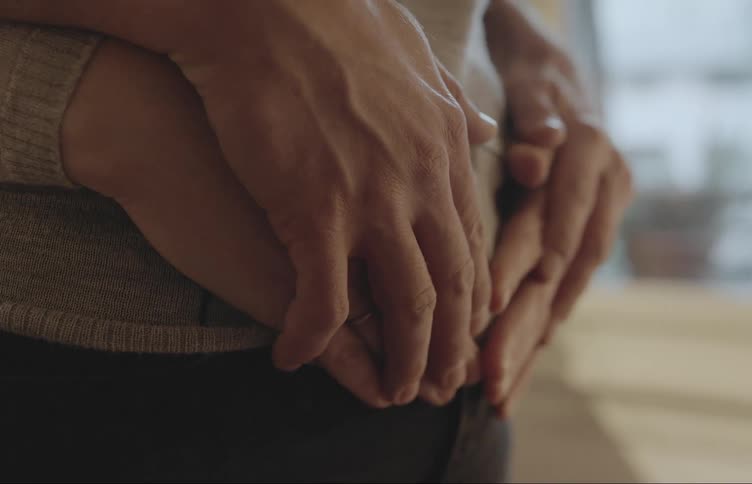 Man placing his hands on his mother his pregnant wifes belly and she placing her hands on top of his
