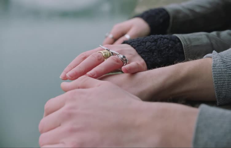 A womans hands side by side with a mans hands as they watch a river in a city then she puts her hand on his