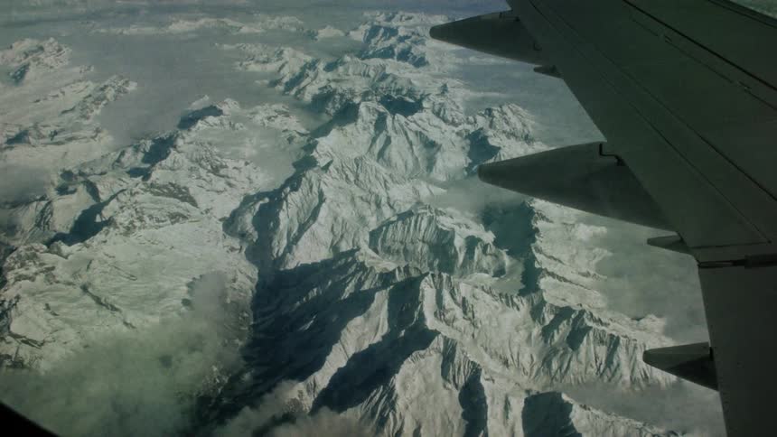 The wing of an airplane as it flies over icy mountains