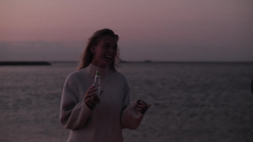 A woman stands out door laughing while holding a beer