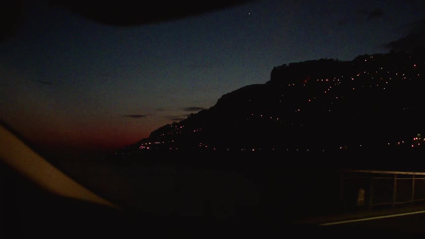 View from inside the car from the windshield with night view of the silhouette of a city over hills
