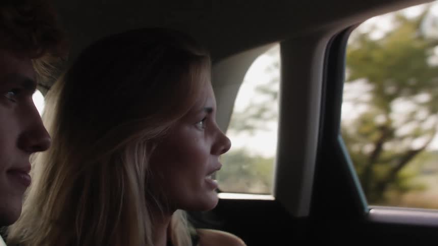 Man and woman seated in a moving car talking while looking outdoor