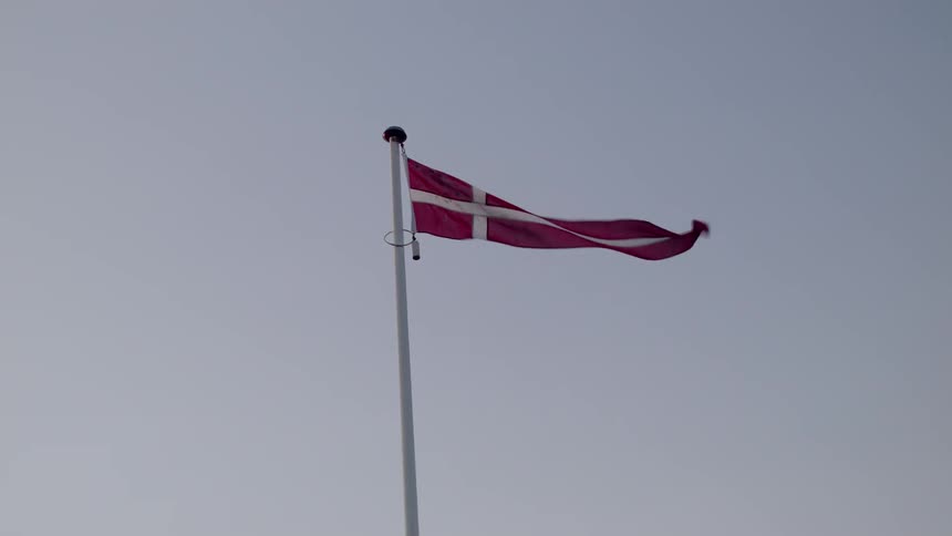 The wind blows strongly and causes a danish flag to flap and flutter