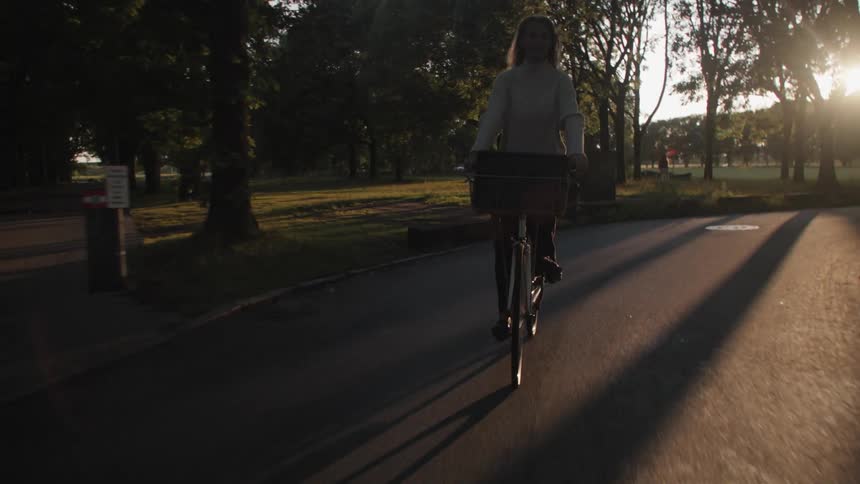 Young woman riding a bicycle in the middle of a park with a reflection of the sun
