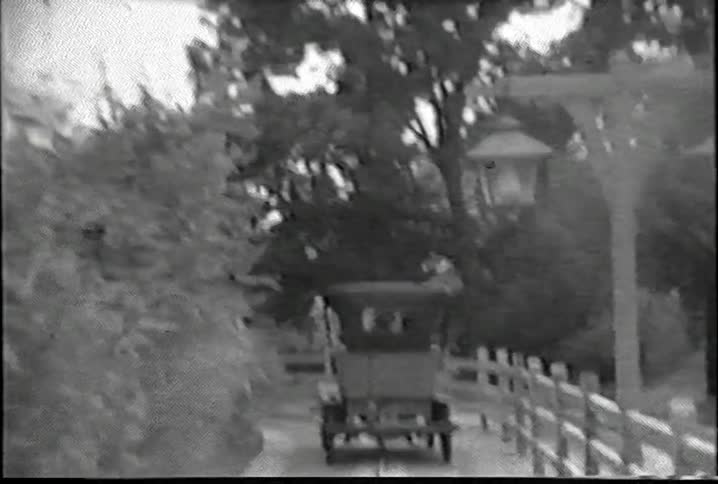 An old jalopy drives down a narrow country road