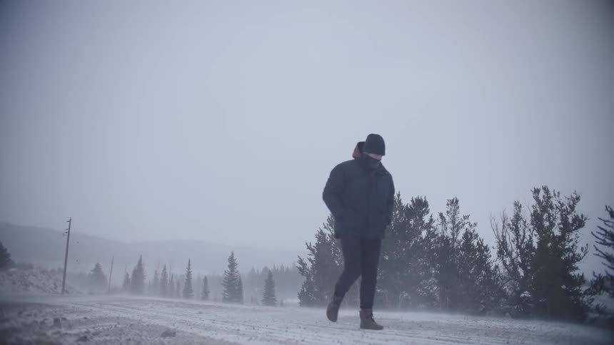A man walks along a rural road during a blizzard