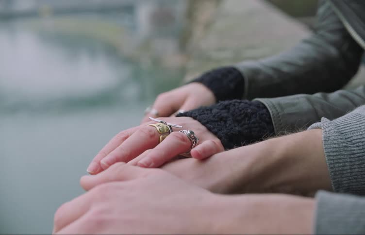 A woman puts her hand on the hand of the man beside her watching a river