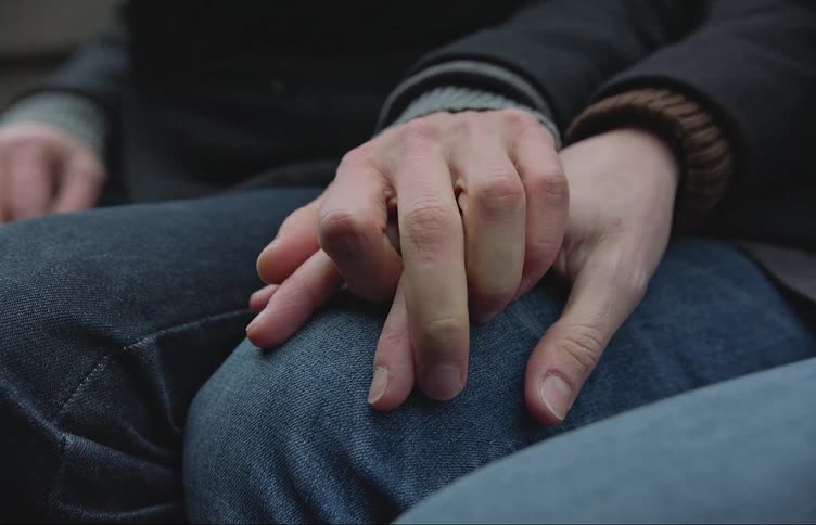 Two people sitting together holding each other hands over their laps