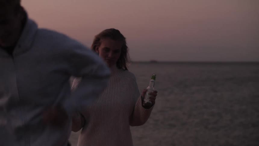 A woman dancing and drinking on the beach during sunset